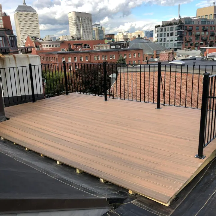 Composite decking and black metal railing finished on a flat roof, high-rise towers in the background