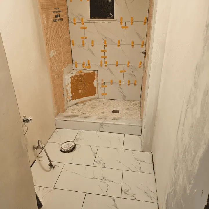 Large-format shower wall tile going up with leveling clips, marble-look floor tile set