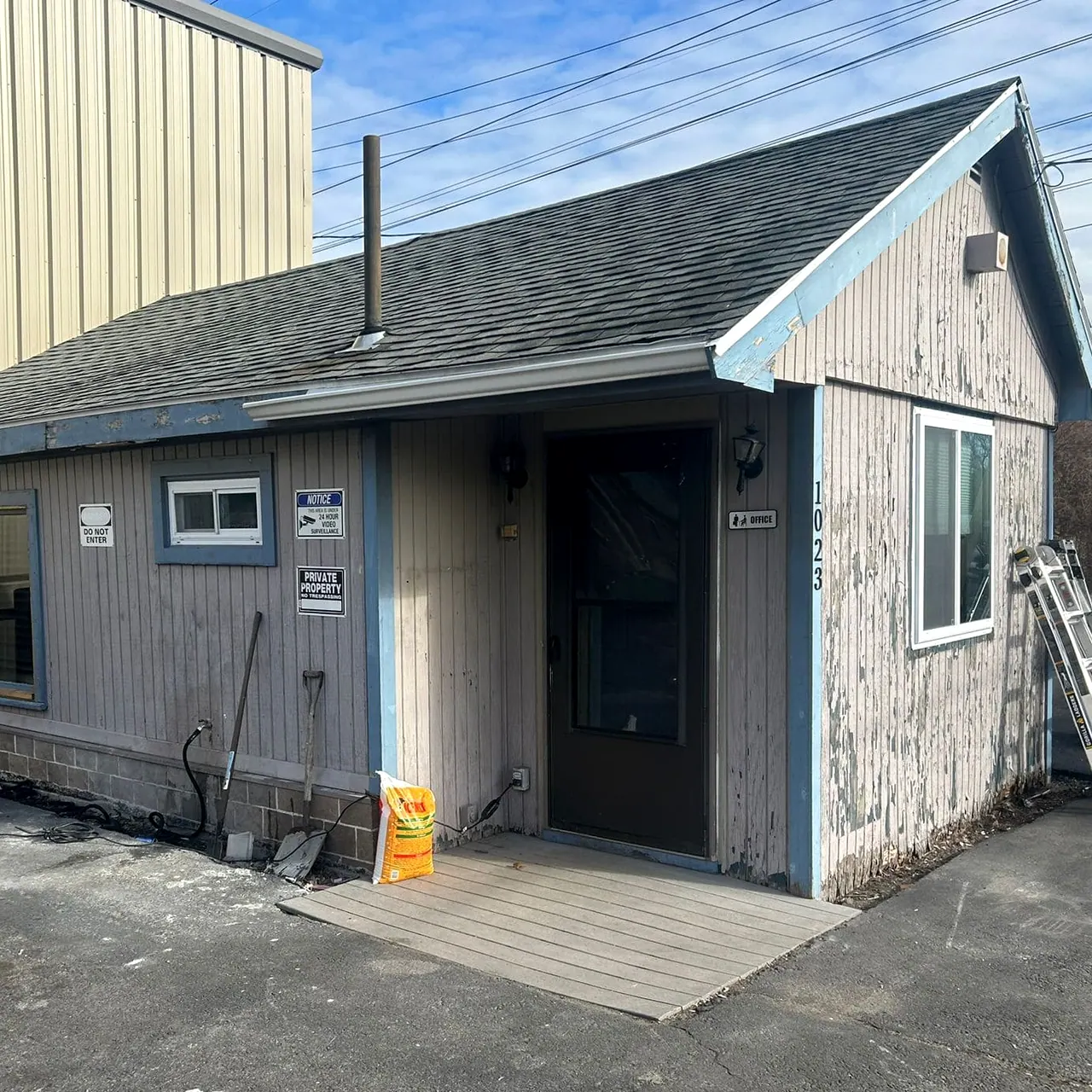 Small single-story building with weathered gray siding, faded blue trim and an old door, before the job