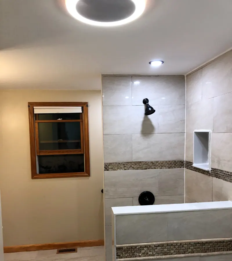 Finished walk-in shower with large-format tile, a mosaic band, a recessed niche and recessed lights